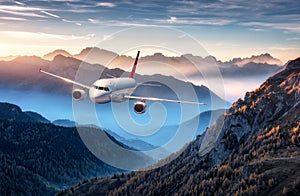 Airplane is flying over mountains in fog at colorful sunset