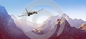 Airplane is flying over mountains in fog at sunset in summer