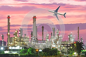 Airplane flying over oil refinery industry plant along twilight