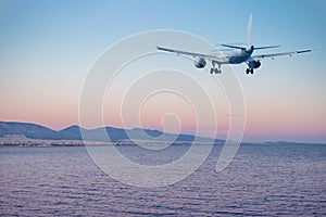 Airplane flying over the sea and beach at sunset.