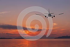 Airplane flying over tropical sea at beautiful color sunset or s