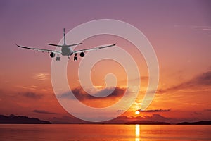 Airplane flying over tropical sea at beautiful sunset or sunrise