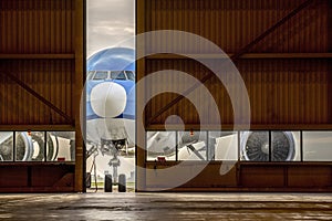 Airplane in front of half opened door to hangar