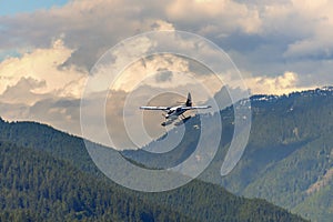 airplane, hydroplane flies in mountains covered with forest, under pink evening clouds