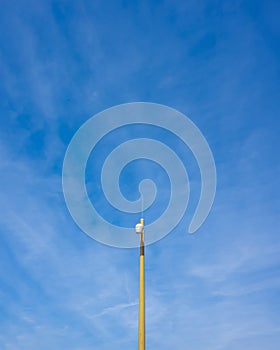 An airplane with its contrail aligned with a yellow lamp-post against a blue sky