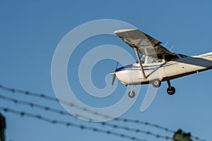 Airplane landing at an airport over a barbed wire fence at sunset.