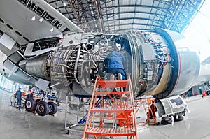 Airplane mechanic diagnose repairs jet engine through open hatch.