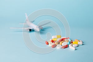 Airplane model with multi-colored pills from motion sickness scattered on a blue background.
