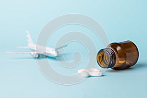 Airplane model with white pills from motion sickness scattered from a glass jar on a blue background.