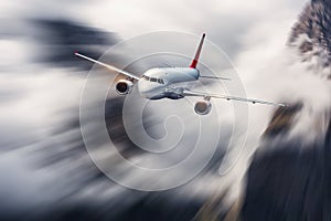 Airplane in motion. Aircraft with motion blur effect is flying in clouds against mountains. Passenger airplane