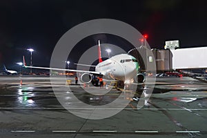 Airplane at passenger gangway of the terminal building at the airport at night, aircraft flight maintenance.