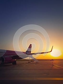 Airplane ready for boarding and takeoff at the airport with the view to the sunrise. Morning travel and holiday concept