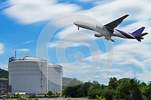 Airplane in the sky over storage tanks at oil terminal with blue