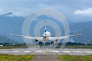Airplane touching down the runway. Mountains and clouds background.