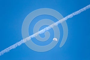 Airplane trails on a blue sky visible moon