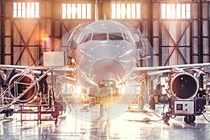 Airplane under repair in the aerospace hangar in the background of the gate and bright sunlight