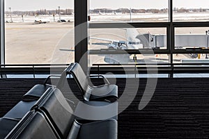 Airplane, view from airport terminal with empty seats in the airport waiting room near the gate. Travel concept