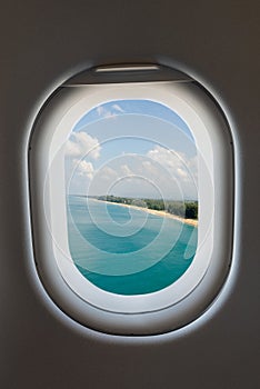 Airplane window from interior of aircraft and tropical beach.