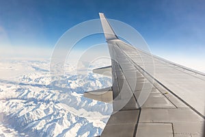 Airplane window seat view while flying over snowy mountains