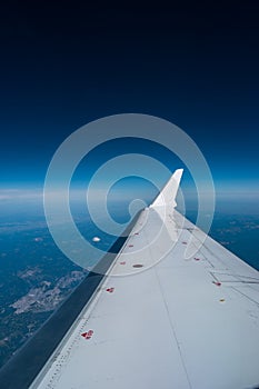 Airplane window view of blue sky and earth with visible white wing in frame