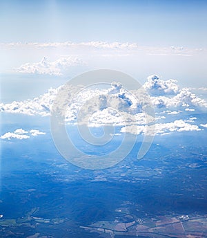 Airplane window view of land and blue sky with clouds