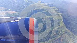 Airplane window view showing wing of the plane flying over land.