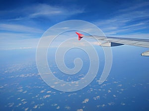 The airplane wing above the blue cloudy sky