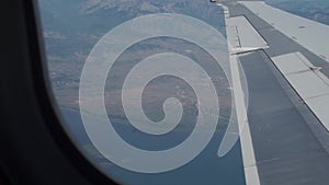 Airplane wing in air. Down in the far land, land coastline, sea in the background