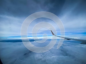 Airplane wing in the blue sky and clouds as seen through window of an aircraft