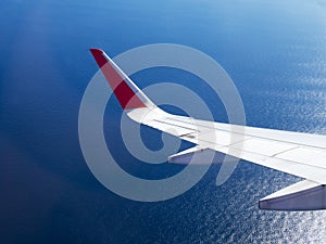 Airplane wing flight flying in sky over blue sea and reflect with sun light. Travel concept