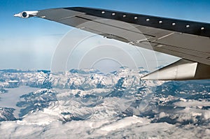 Airplane wing flying above snowy mountains