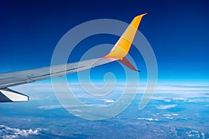 Airplane wing flying high in the atmosphere against the background of blue air. White-orange plane in the sky above the clouds and