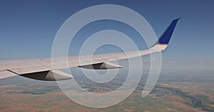 An airplane wing is flying over a fluffy cloudy sky as seen from the window of an airplane on land in the background