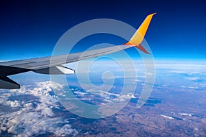 Airplane wing flying over white clouds and brown earth in a blue atmosphere