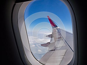 Airplane wing over blue sky and white cloud view looking through airplane window. Travel, vacation and journey concept