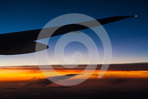 Airplane wing over clouds at sunset