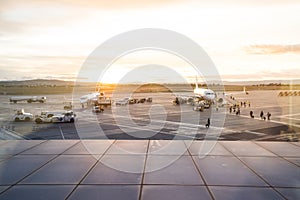 Airplanes on the airport runway. Operators loading and unloading and people boarding the planes. Airport at sunset