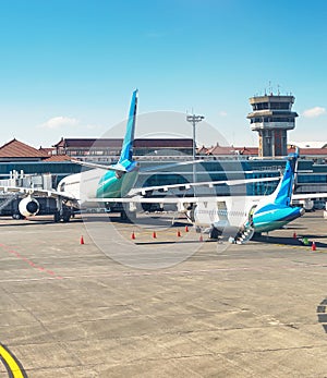 Airplanes and truck at runway in morning sunlight, Denpasar airport building, Bali, Indonesia