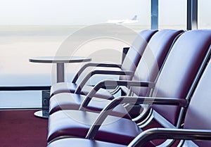 Bench in departure flights waiting hall at the airport with airplane in the background