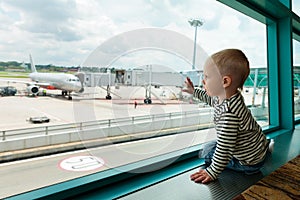 In airport hall child looks at the plane through window