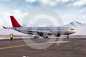 Airport marshaller meets passenger airliner on the background of high picturesque mountains photo