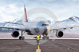 Airport marshaller meets passenger jetliner on the background of high scenic mountains photo