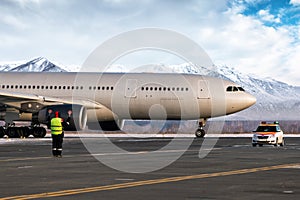 Airport marshaller meets wide body passenger airplane on the background of high snow covered mountains