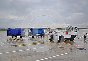 Airport runway vehicle car with trailers full of luggage and baggage covered with waterproof cover on a rainy day