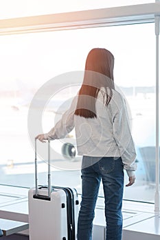 Airport traveller lifestyle of young girl passenger with luggage in airport terminal departure hall area looking out toward