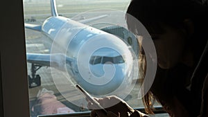 At the airport, in the waiting room, against the background of a window overlooking the airplanes and the runway, sits a