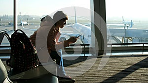 At the airport, in the waiting room, against the background of a window overlooking the airplanes and the runway, sits a