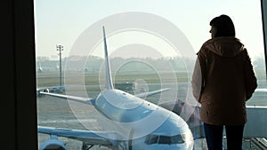 At the airport, in the waiting room, against the background of a window overlooking the airplanes and the runway, stands