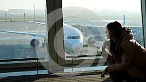 At the airport, in the waiting room, in the background of a window overlooking the airplanes and the runway, a young