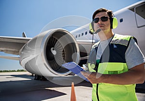 Airport worker with clipboard near giant jet engine